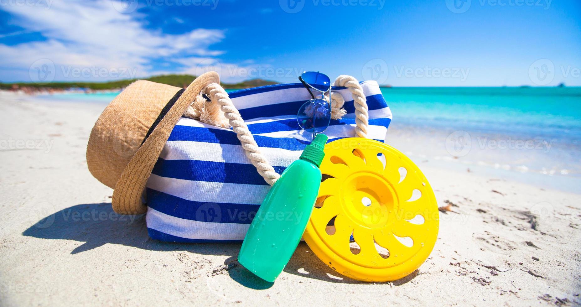 Stripe bag, straw hat, sunblock and towel on white tropical beach photo