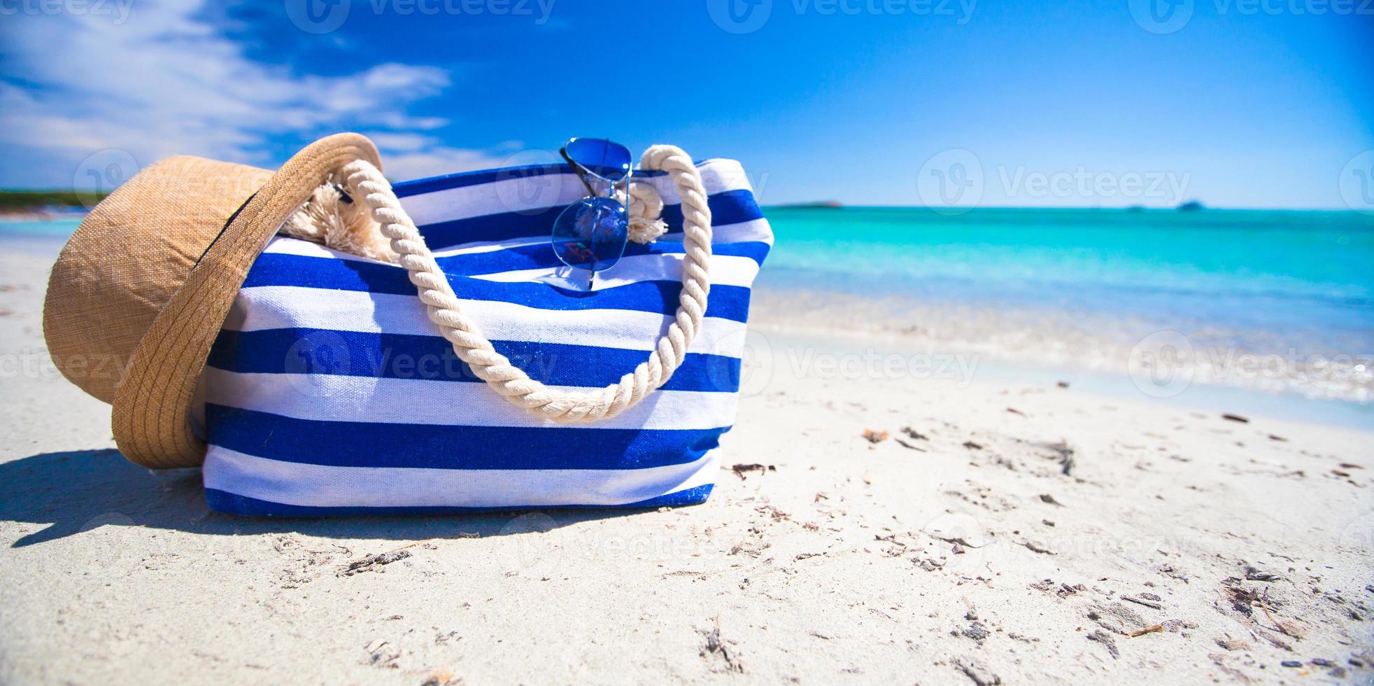 Stripe bag, straw hat, sunblock and towel on white tropical beach photo