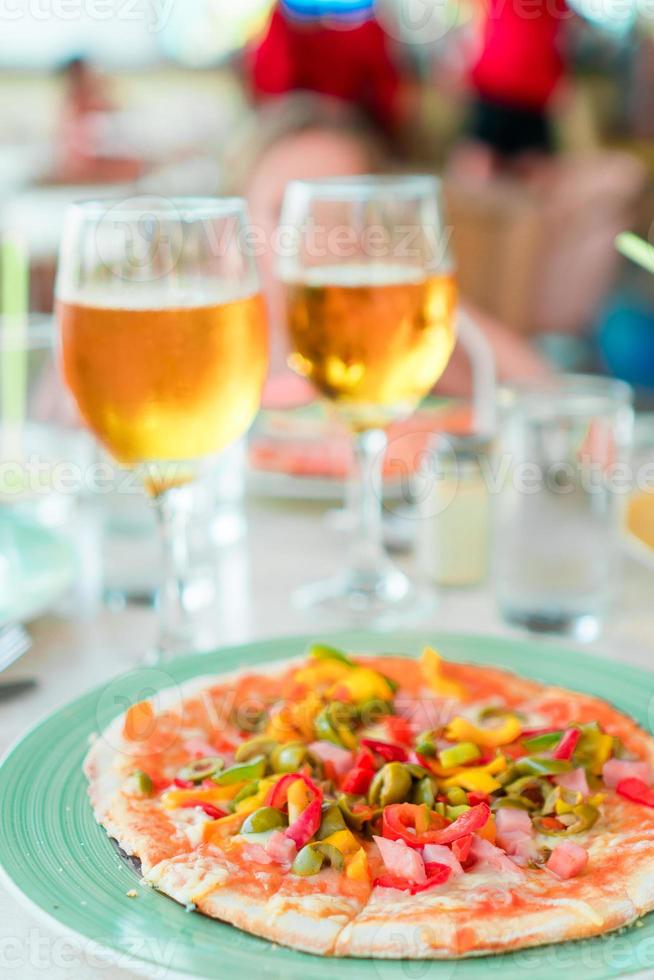 pizza con queso mozzarella, aceitunas, tomate fresco y salsa pesto. servido en la mesa del restaurante con dos cervezas foto