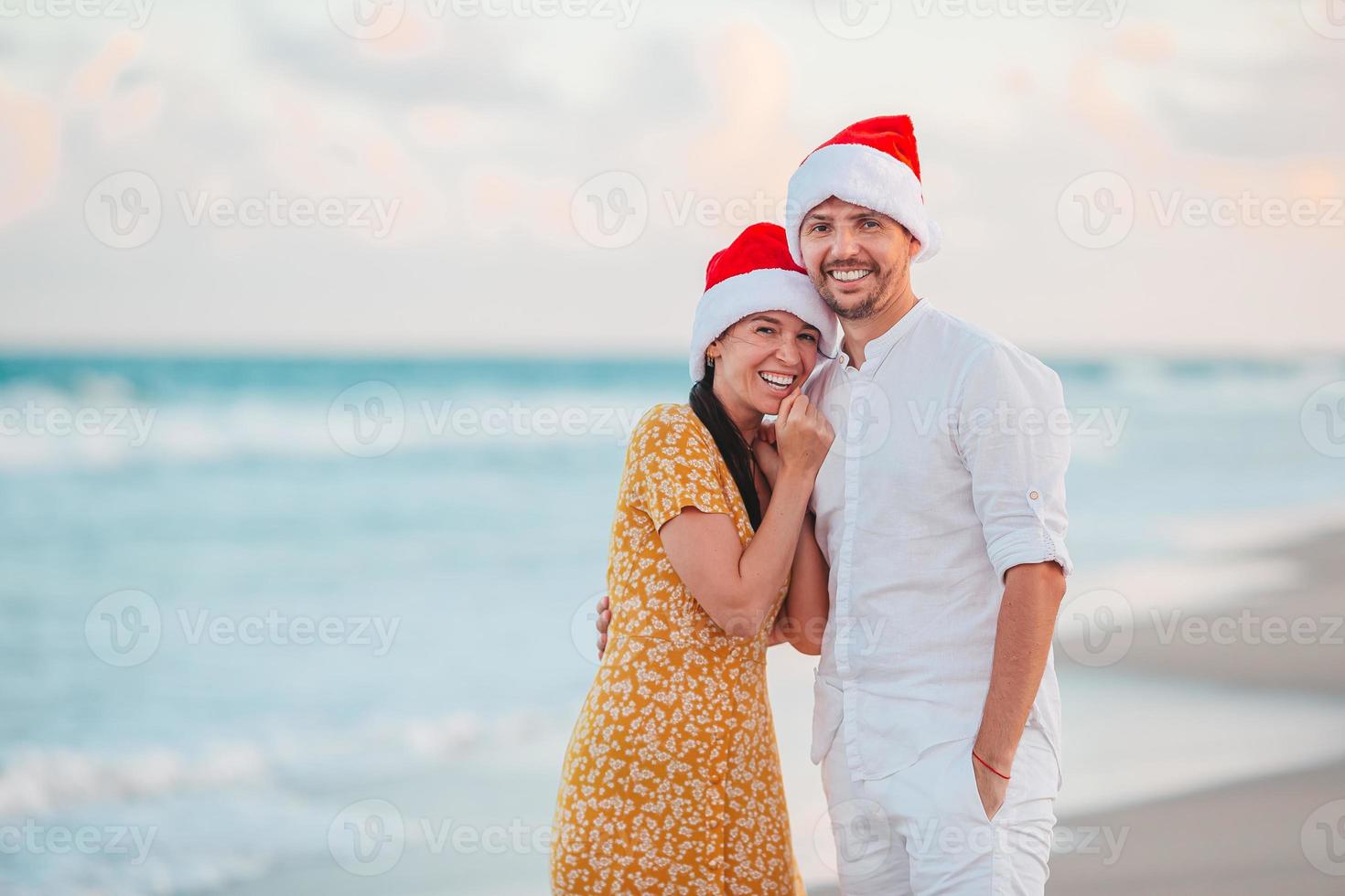 pareja feliz de navidad en sombreros de santa en vacaciones en la playa foto