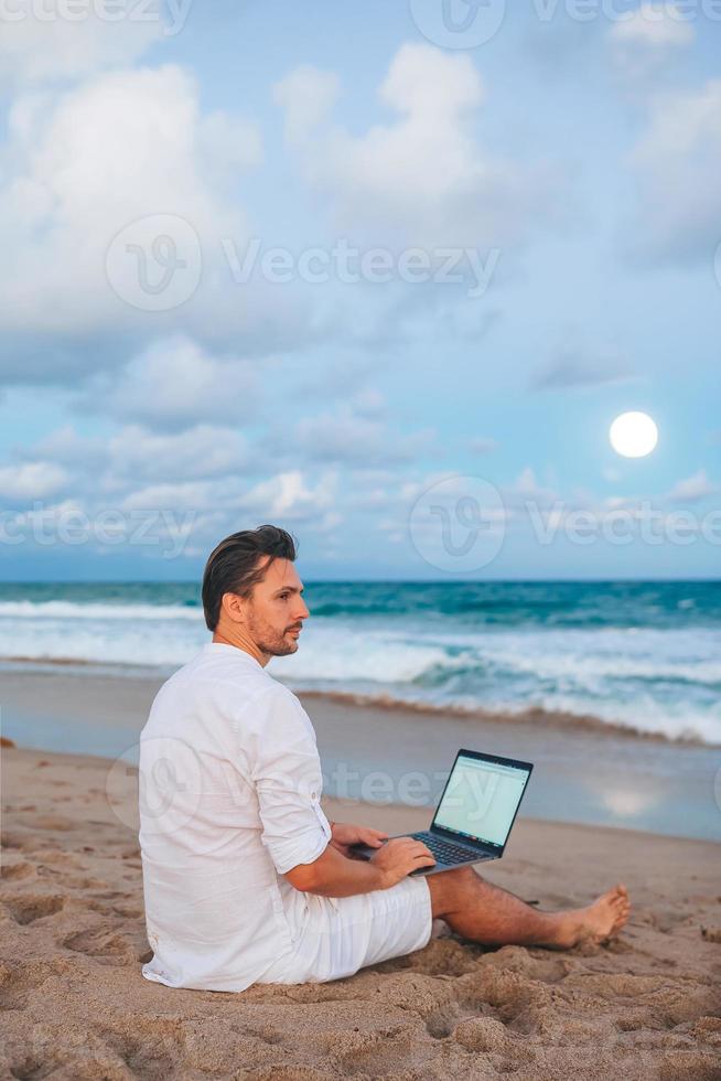 Man with laptop on the beach at sunset photo
