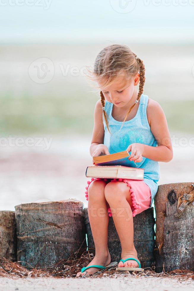 Little adorable girl reading book during tropical white beach photo