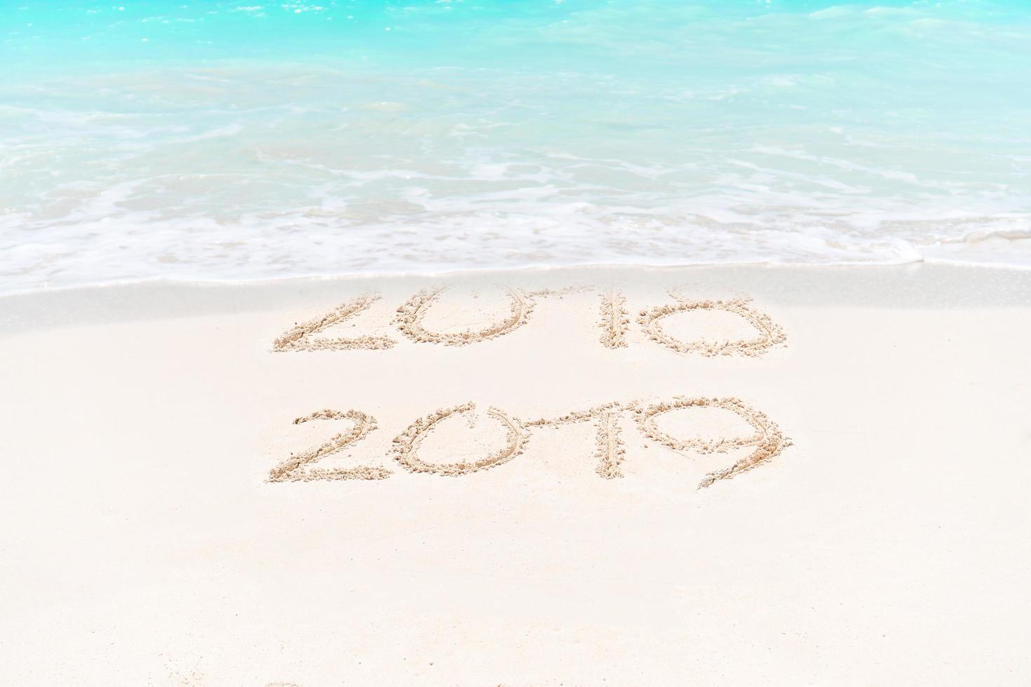 2018 and 2019 handwritten on sandy beach with soft ocean wave on background photo
