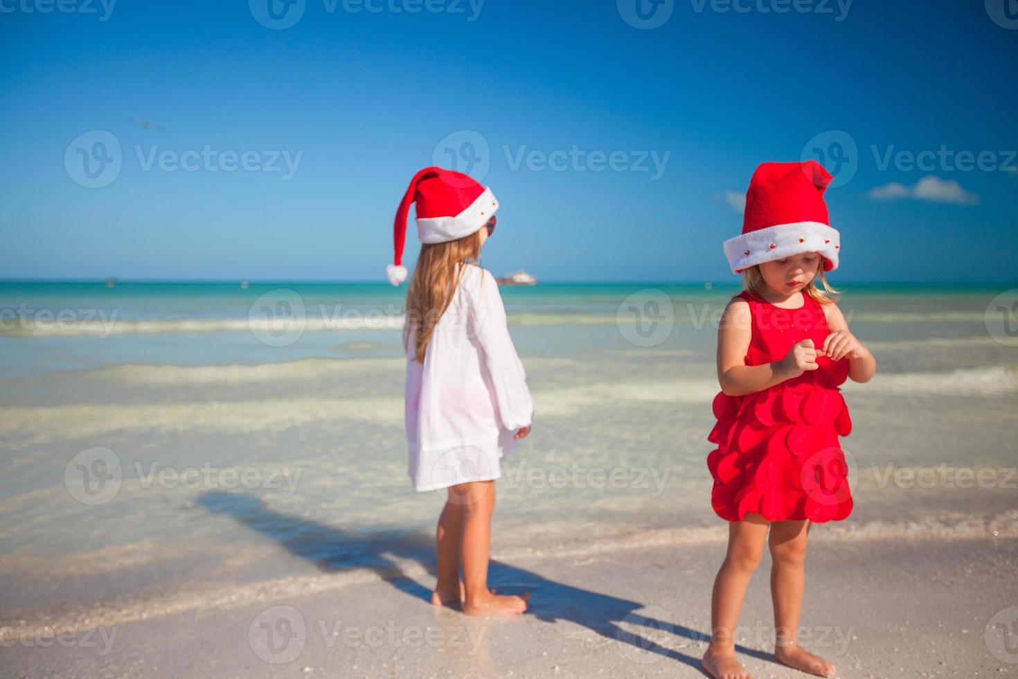 Back view of Little cute girls in Christmas hats on the exotic beach photo