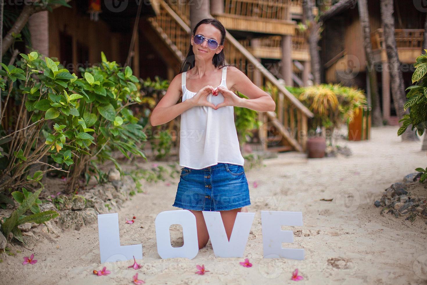 niña sentada en la arena con la palabra amor y haciendo el corazón con la mano foto