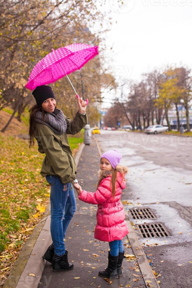 Little girl walking with her mother under an umbrella on a rainy day photo