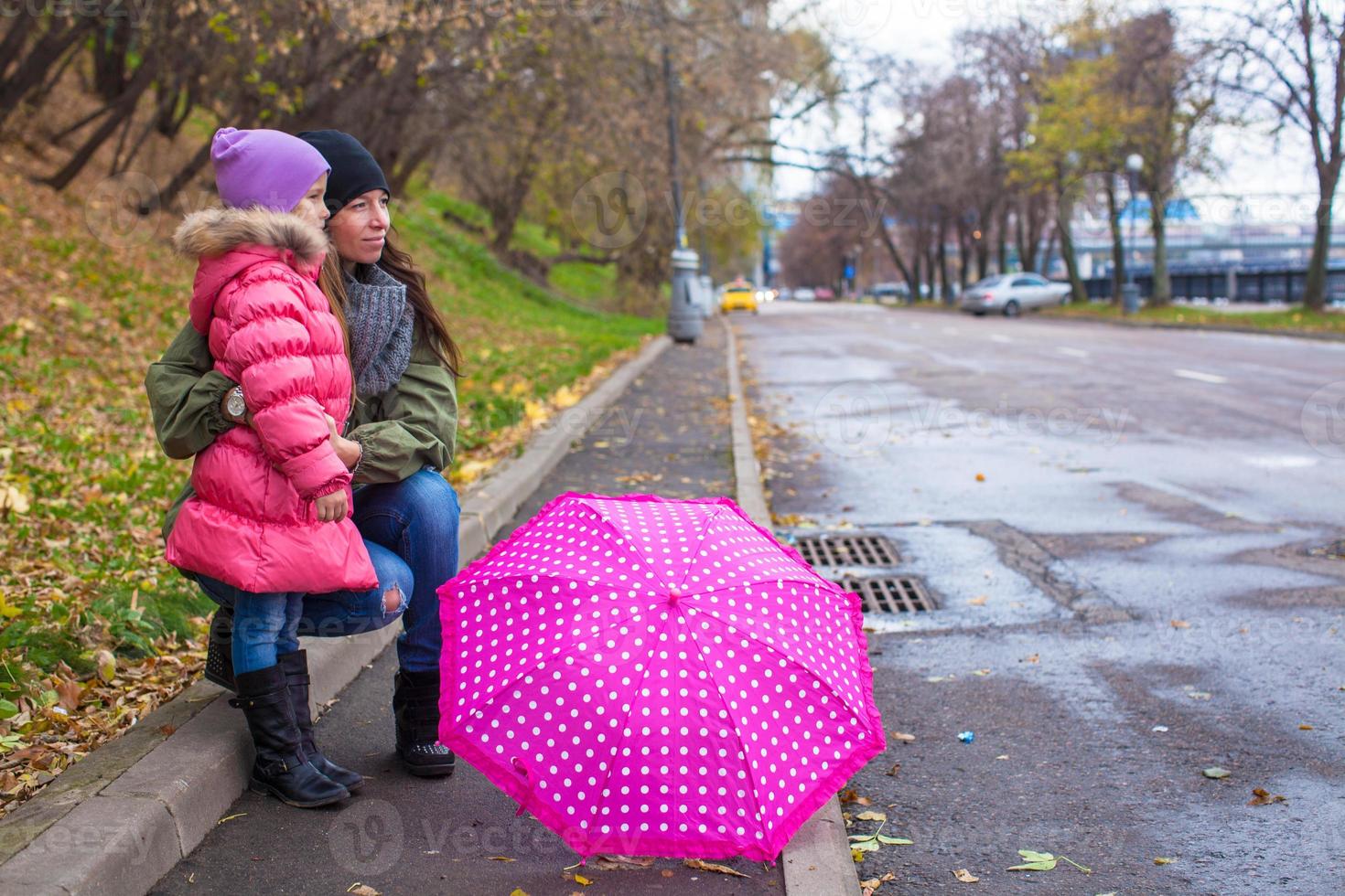 Little girl and her mother walking with umbrella on a rainy day photo