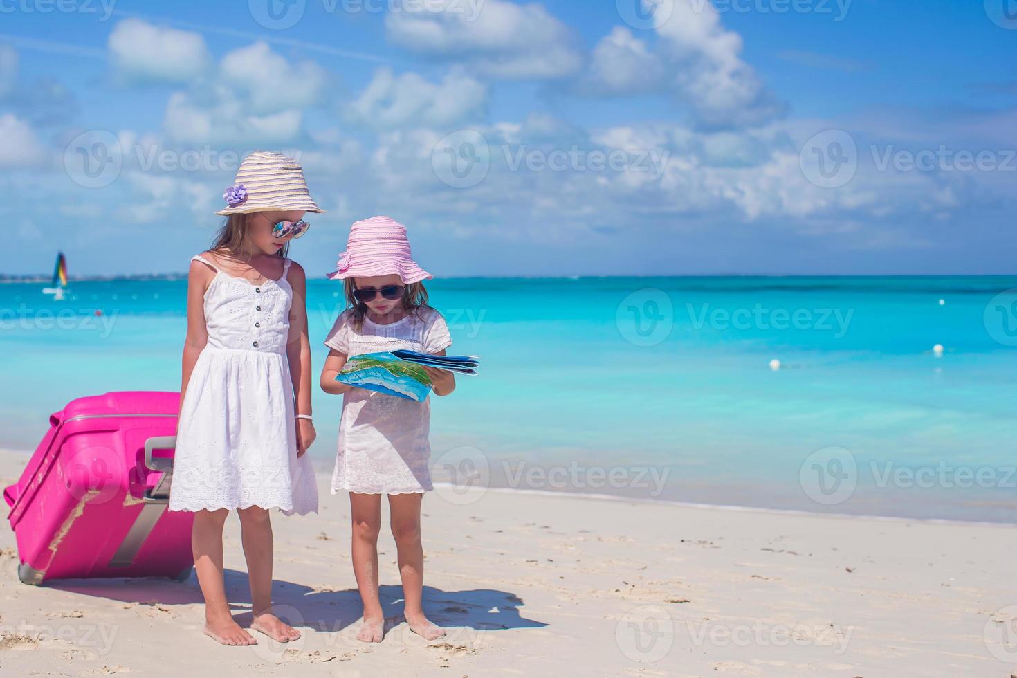 Adorable little girls walking big suitcase and map searching the way on tropical beach photo