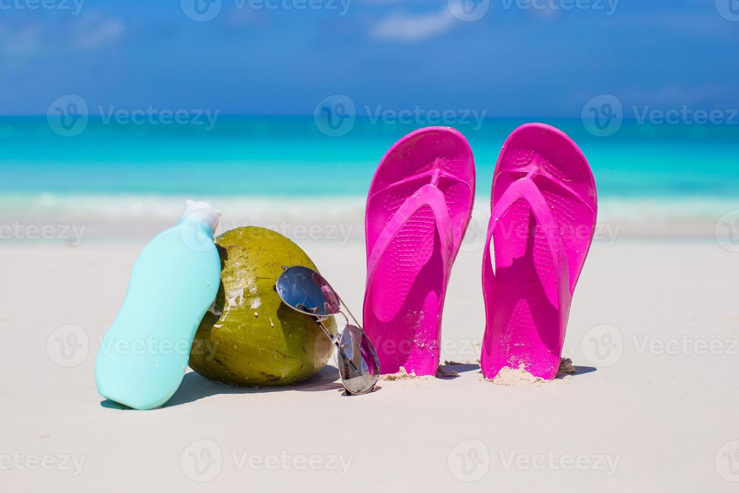 Flip flops, coconut and suncream on white sand photo