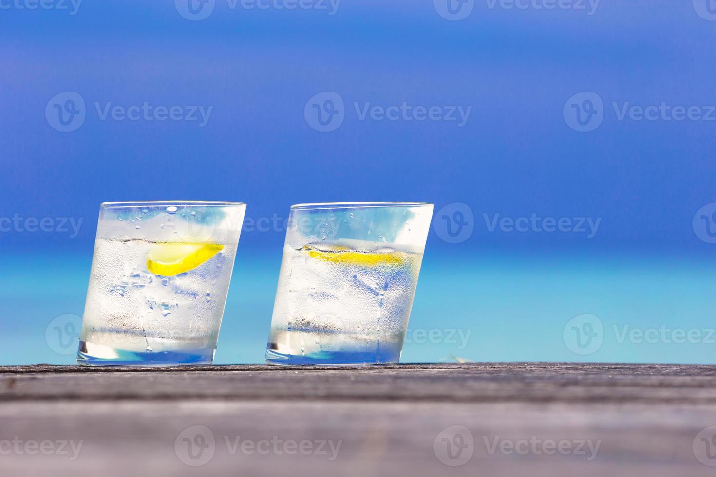 Glasses of waters with lemon on wooden on sea background photo