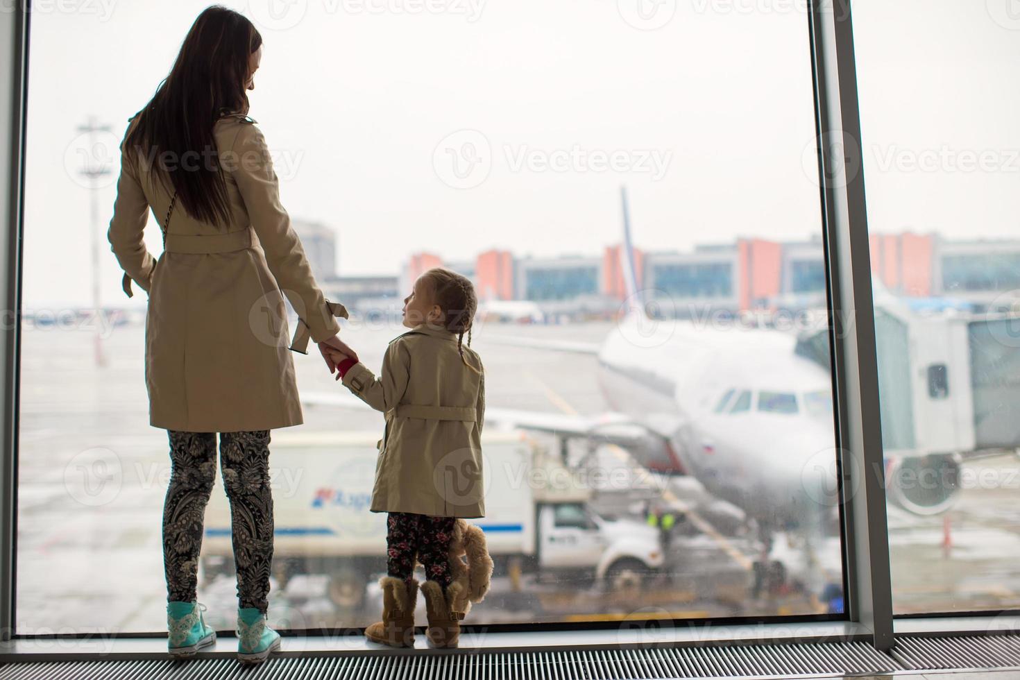 Mother and little daughter looking out the window at airport terminal photo