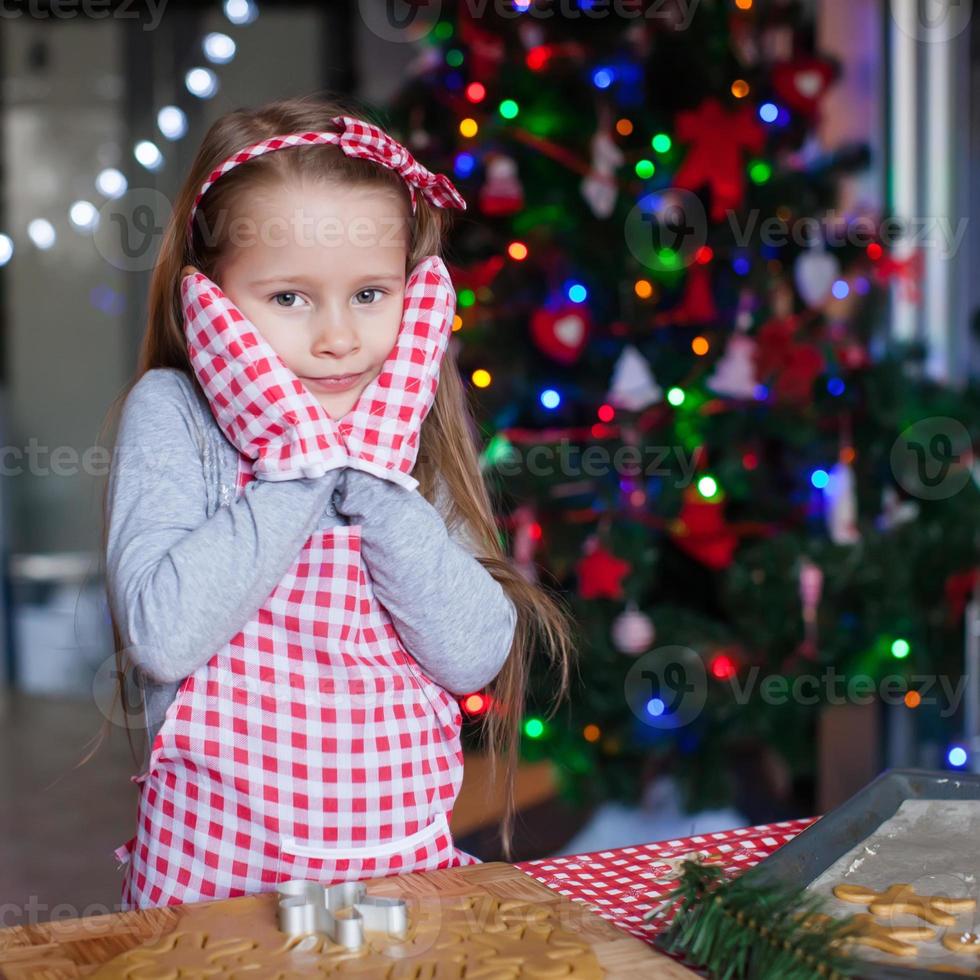 Adorable little girl in wore mittens baking Christmas gingerbread cookies photo