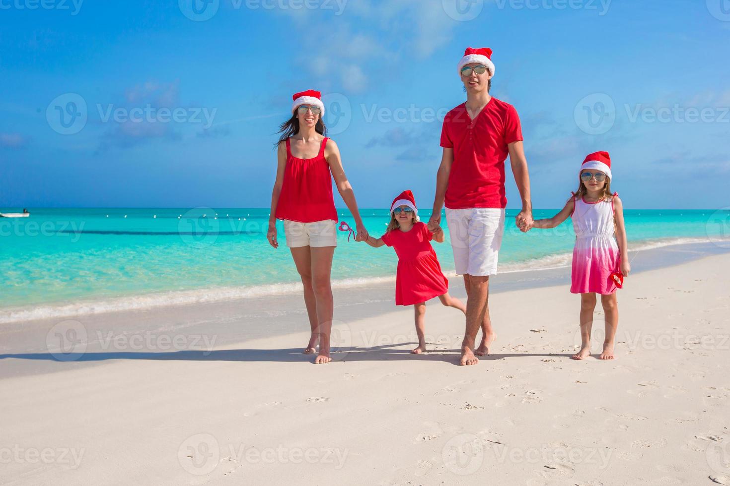 Happy family of four on beach in red Santa hats photo