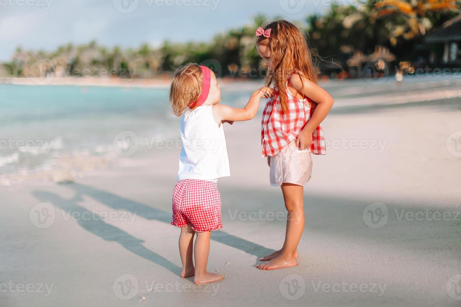 Little happy funny girls have a lot of fun at tropical beach playing together. photo