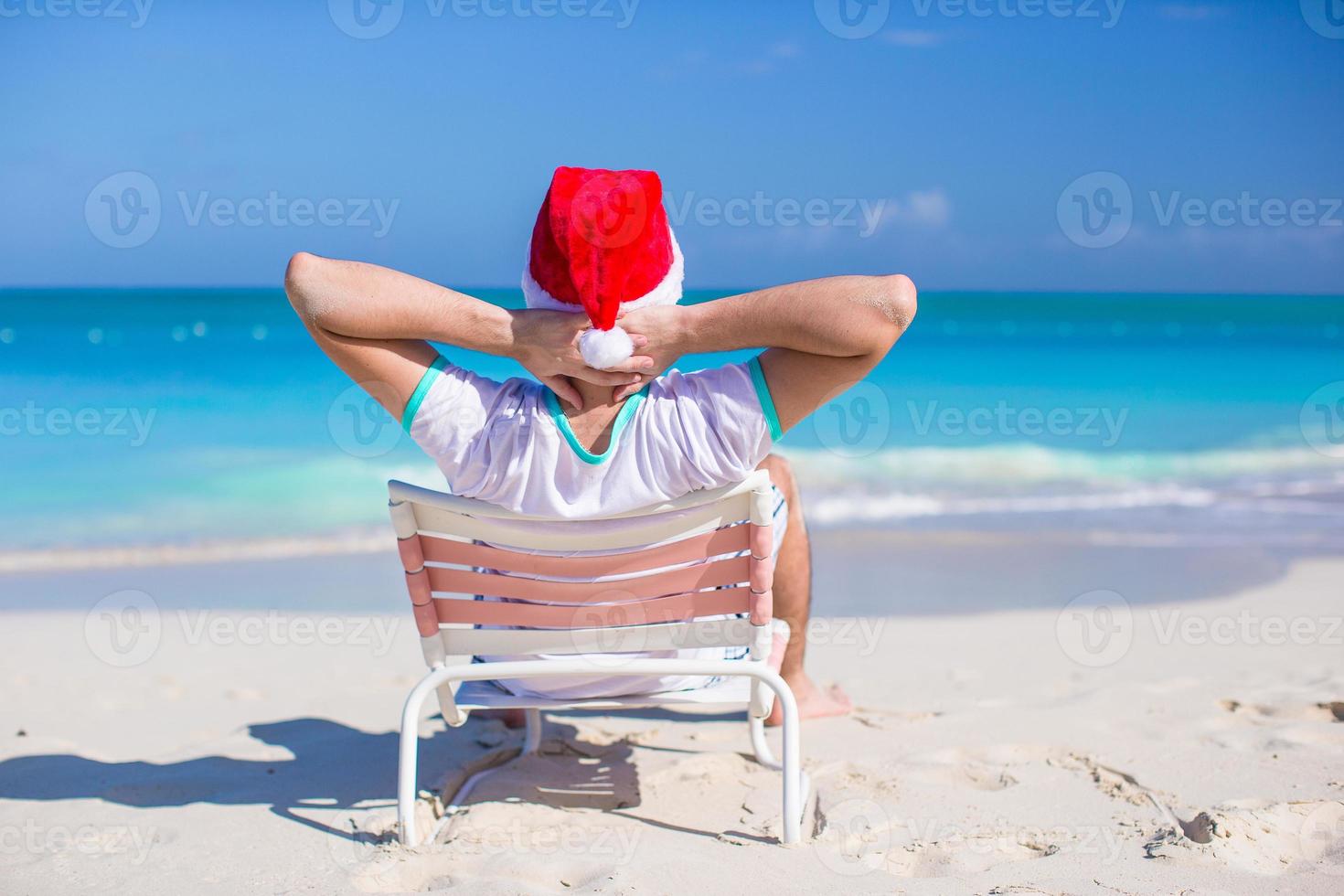 Back view of young man in santa hat relax at beach chair photo
