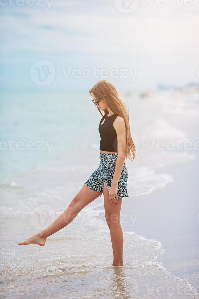 Beautiful teen girl splashing in shallow water while walking on the beach photo