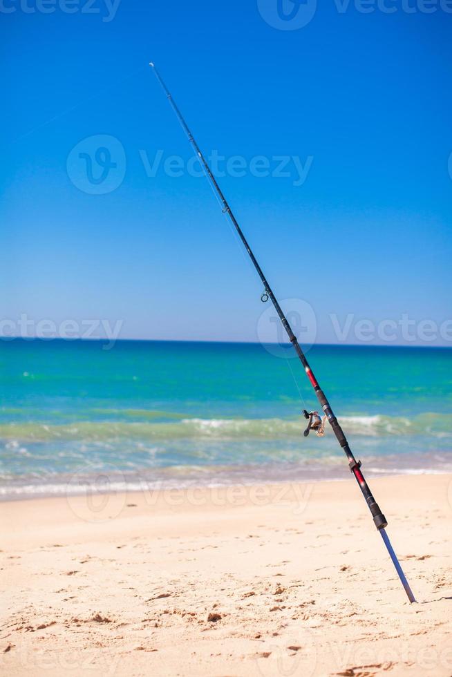 Fishing rod in white sand on tropical beach photo