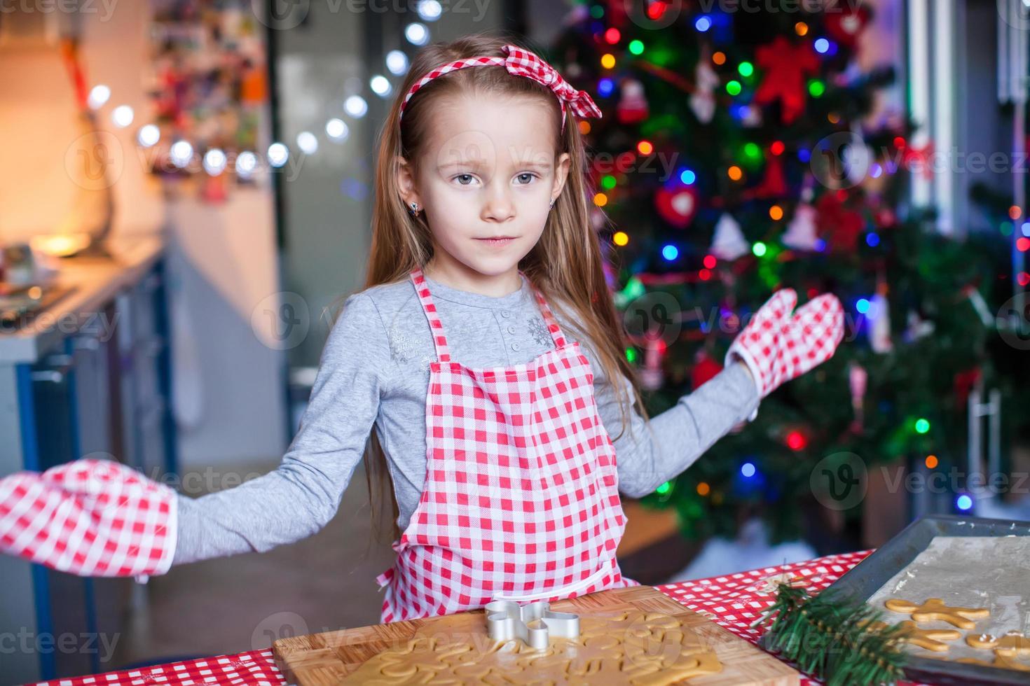 Happy little girl in wore mittens baking Christmas gingerbread cookies photo