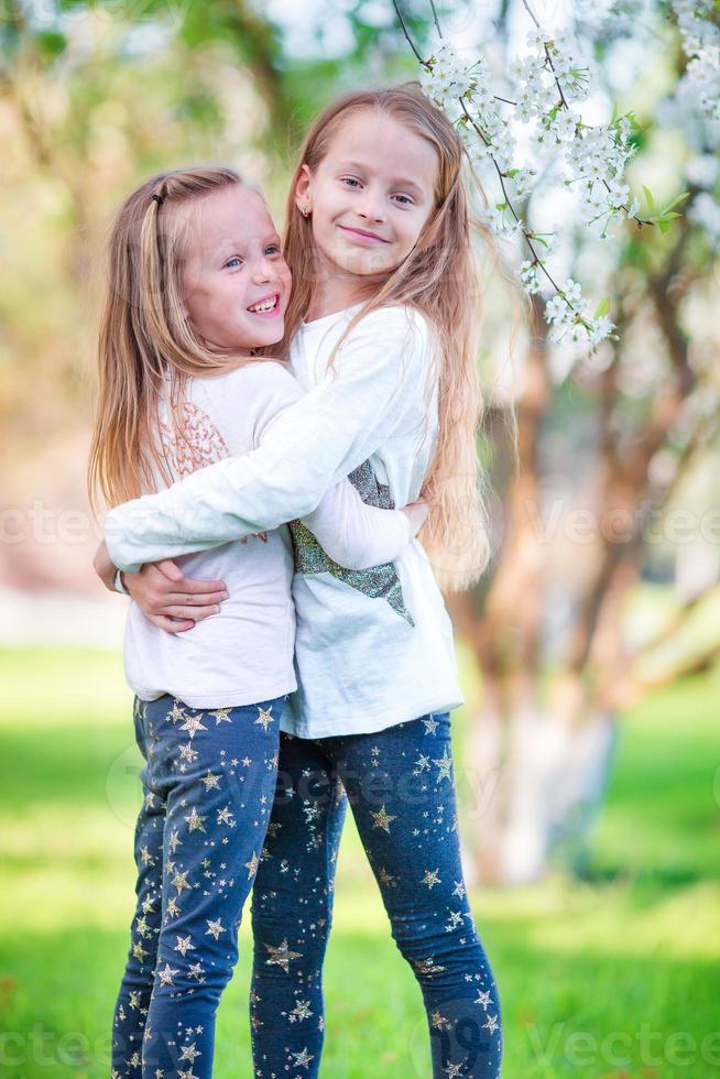 Adorable little girls in blooming cherry tree garden on spring day photo