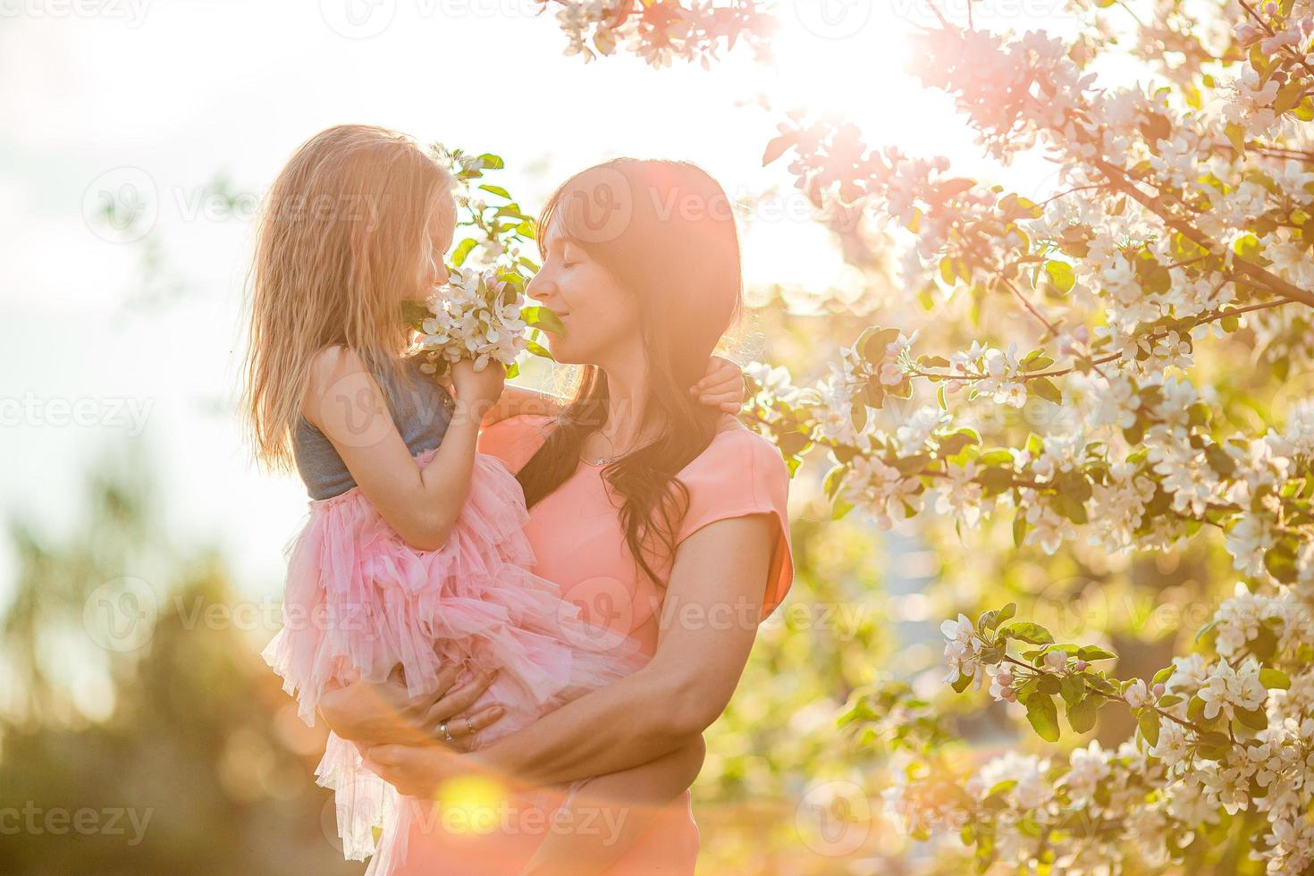 Adorable little girl with young mother in blooming cherry garden on beautiful spring day photo