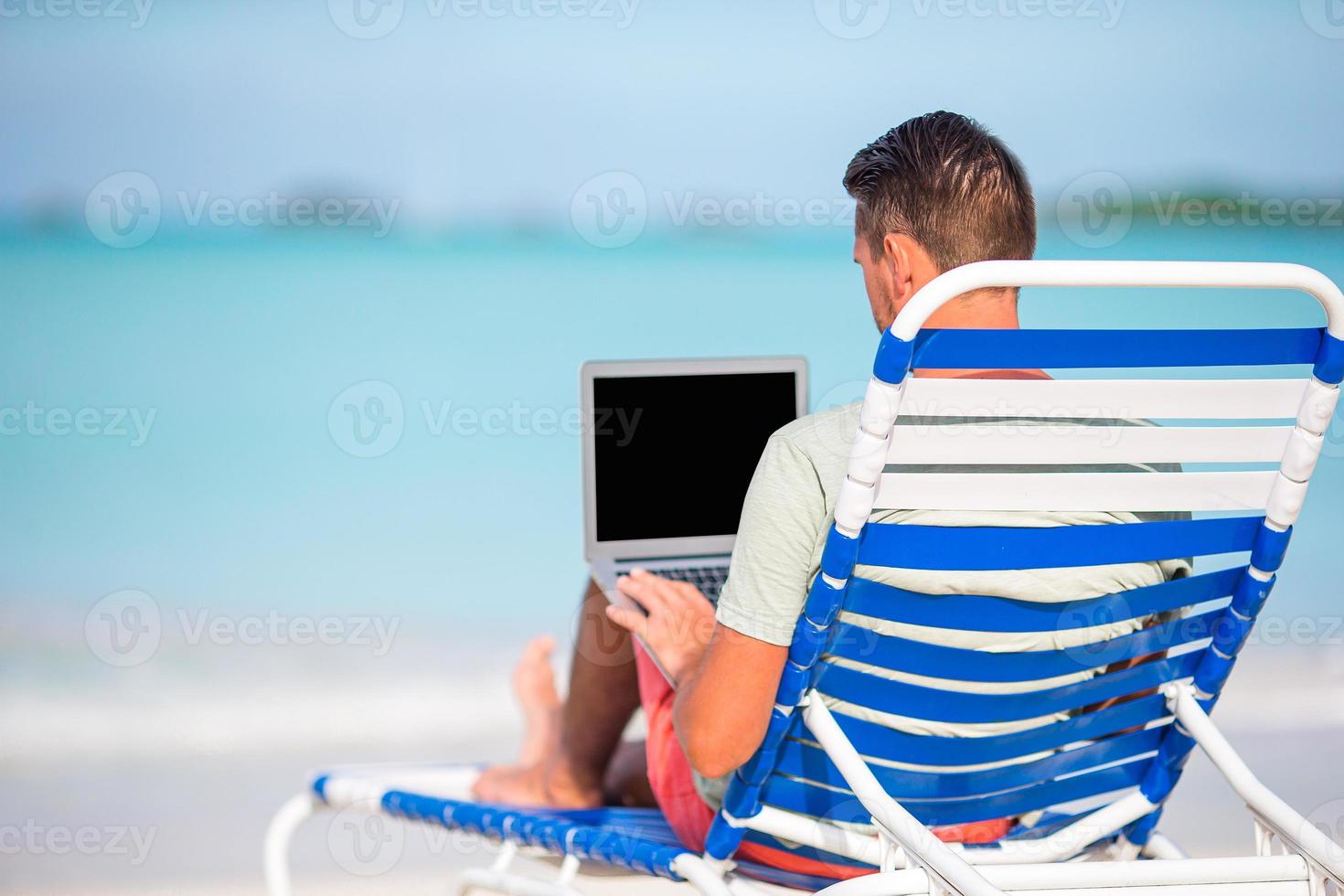 Young man with tablet computer during tropical beach vacation photo