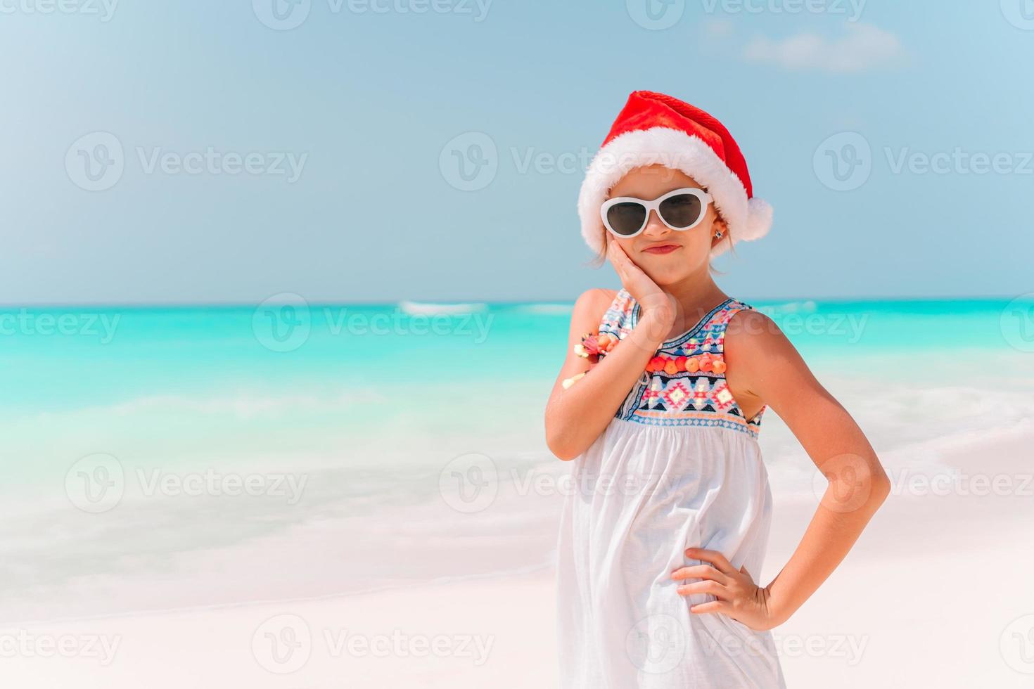 Adorable niña con gorro de Papá Noel en la playa tropical foto