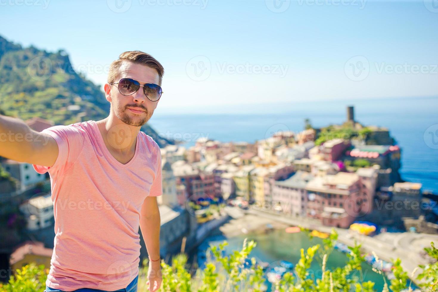 Happy young man taking selfie background the old coastal town of Vernazza, Cinque Terre National Park, Italy photo