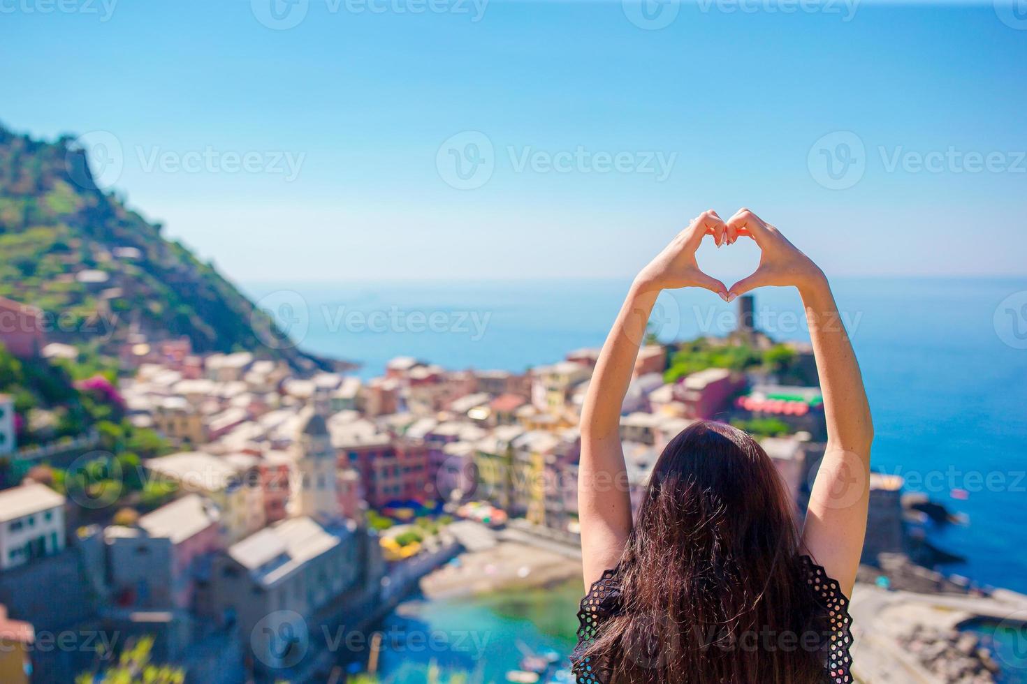 Happy girl making with hands heart shape on the old coastal town background of Vernazza, Cinque Terre National Park. European vacation. photo