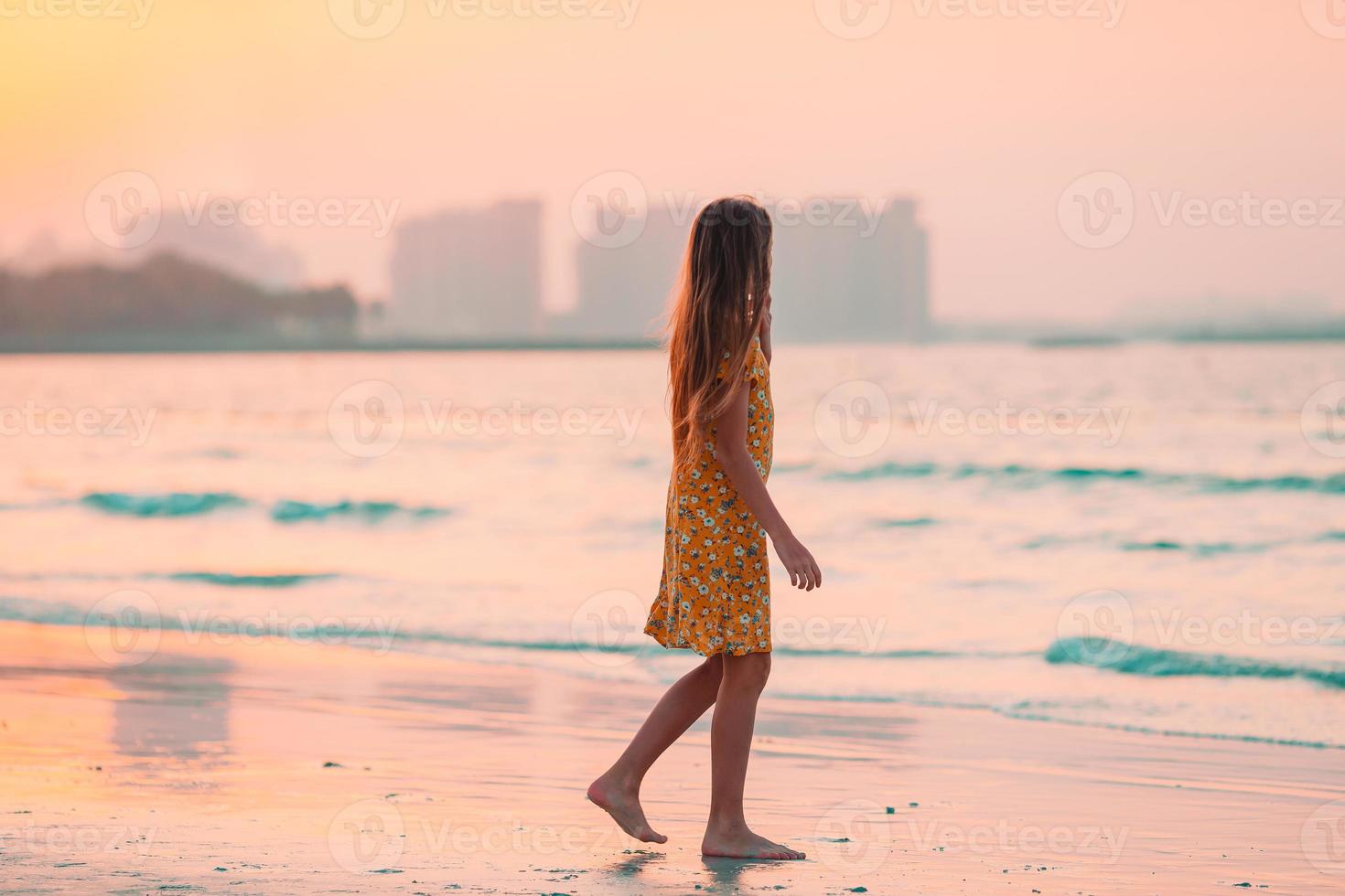 Adorable happy little girl on white beach at sunset. photo