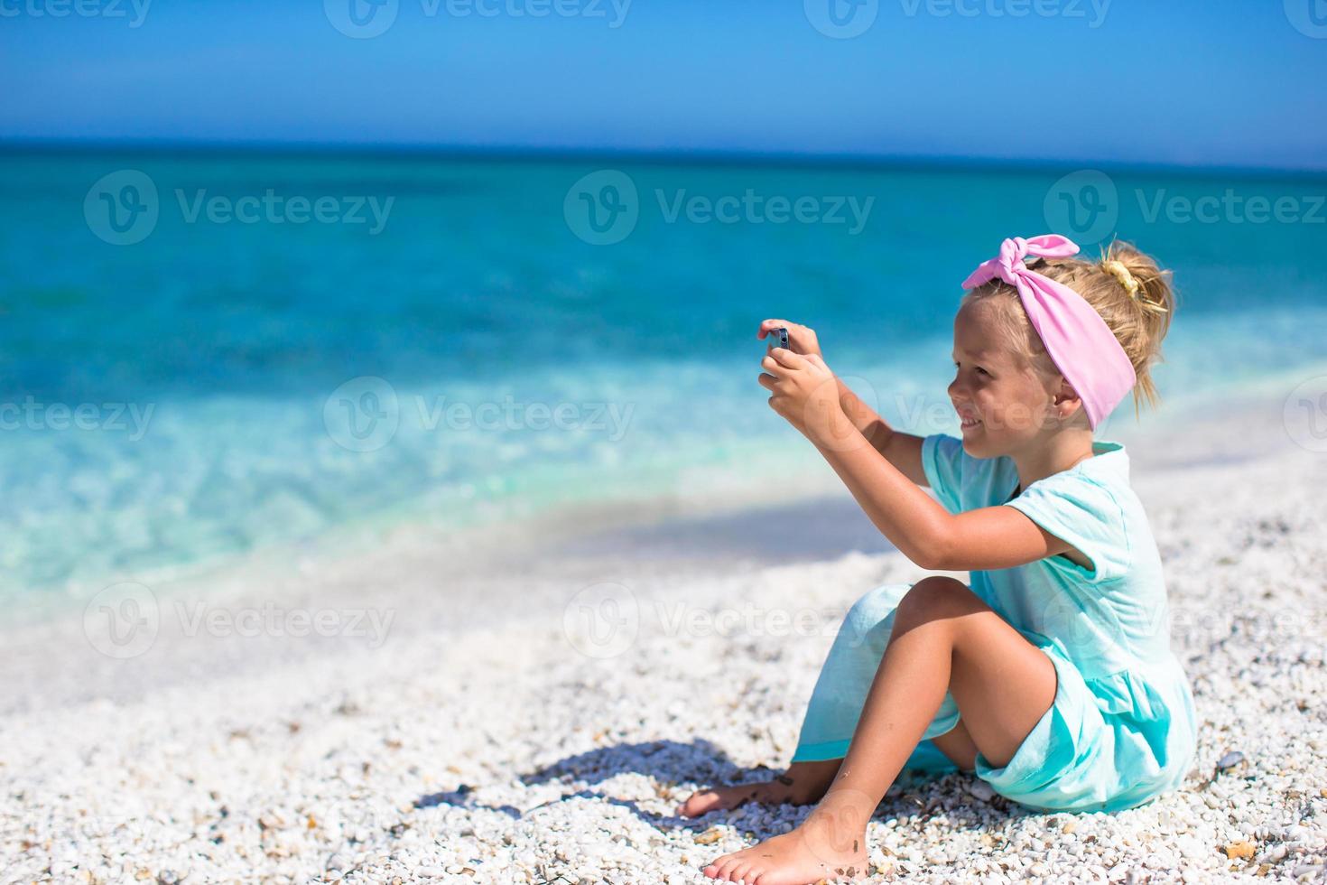 Little cute girl taking pictures on phone at tropical beach photo