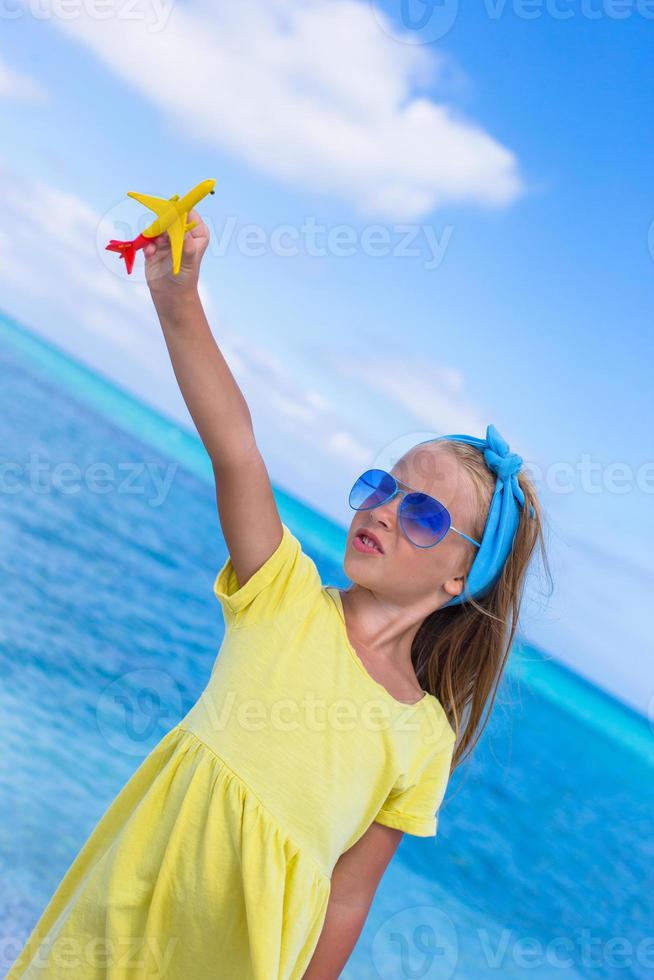 Happy little girl with toy airplane on white sandy beach photo