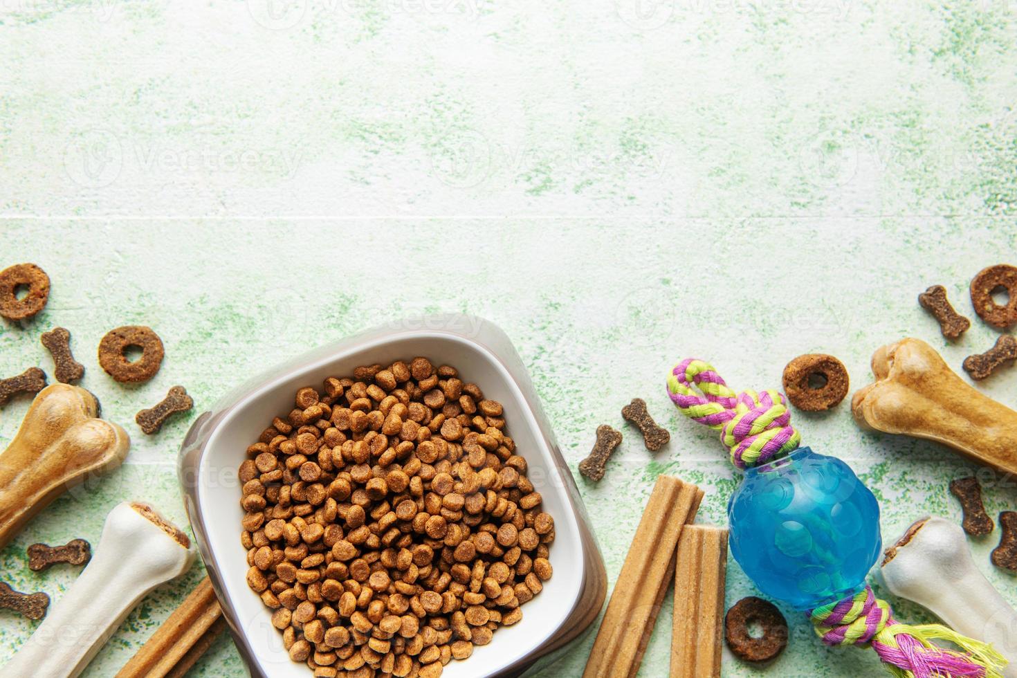 A bowl with dog food, dog treats and toys on a wooden floor. photo