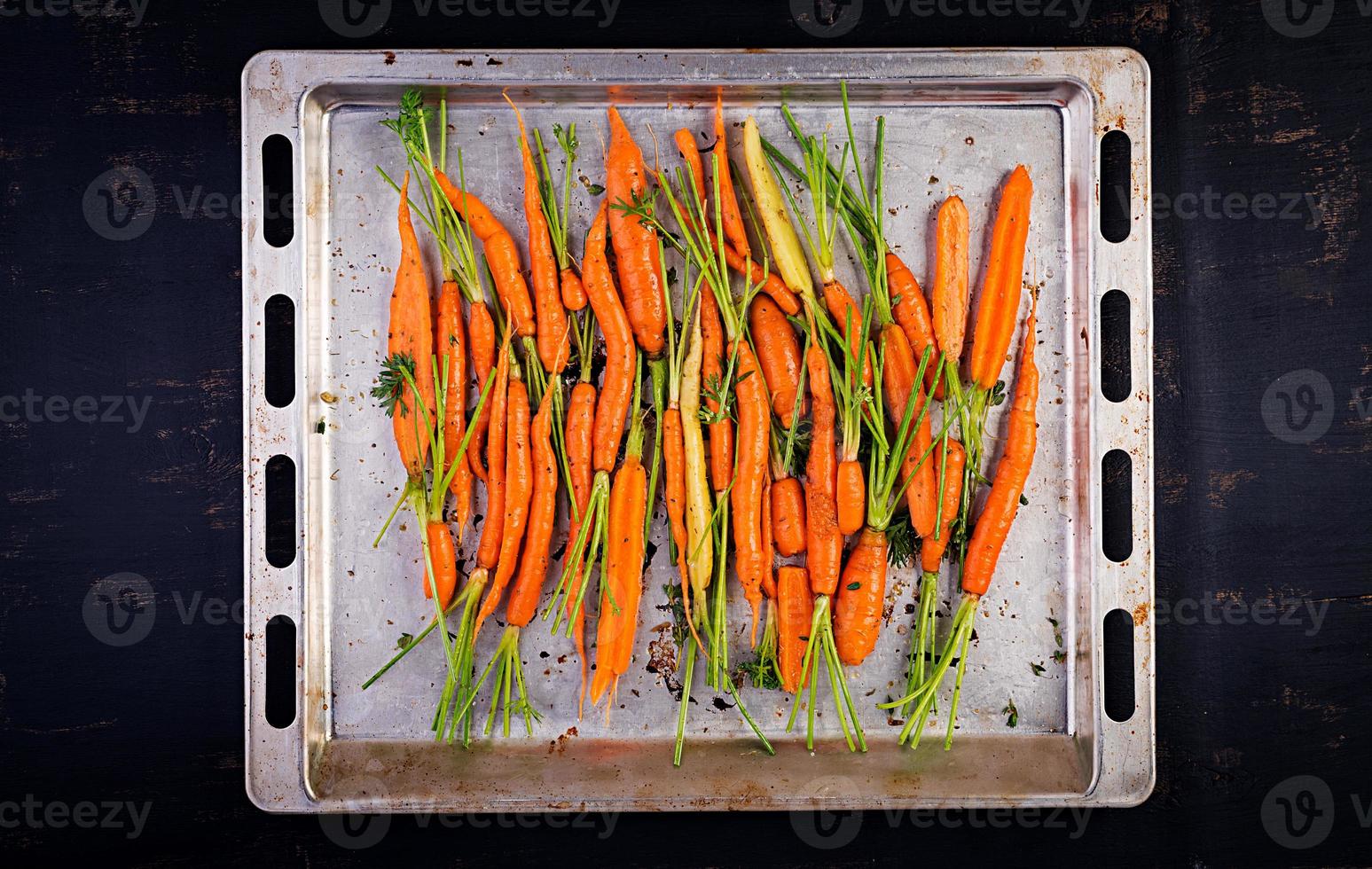 Raw organic carrots with thyme, honey and lemon prepared for roasting on a baking sheet. Organic vegan food. View from above photo