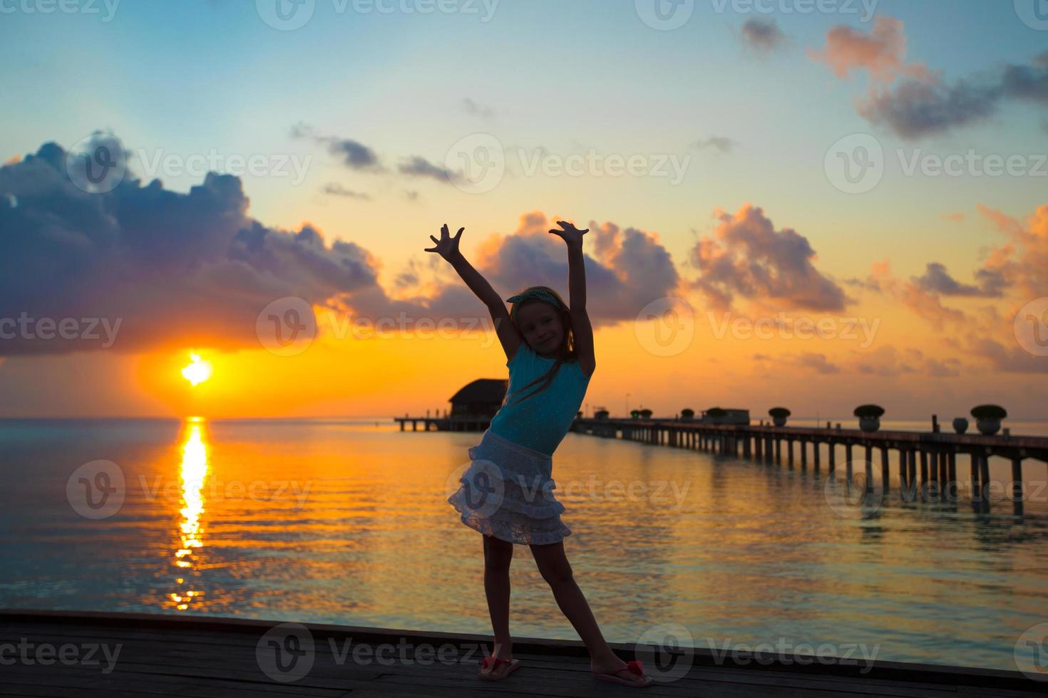 Silhouette of adorable little girl on wooden jetty at sunset photo