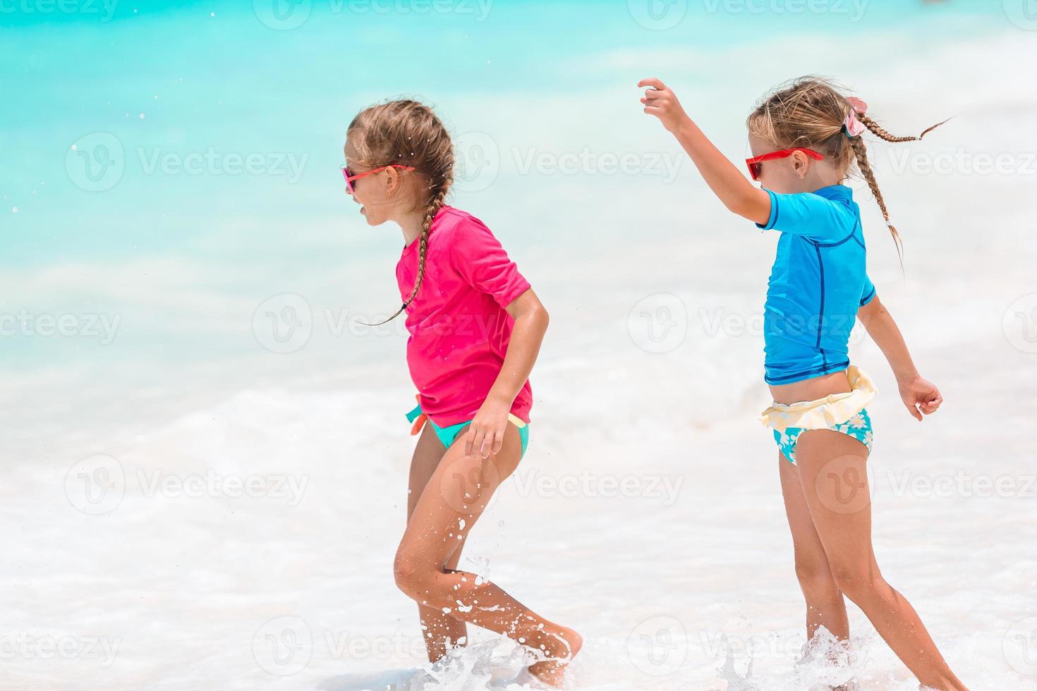 Little happy funny girls have a lot of fun at tropical beach playing together. Sunny day with rain in the sea photo