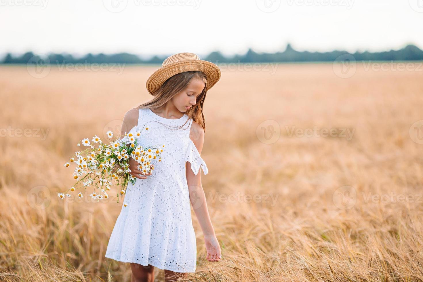 niño feliz en campo de trigo. hermosa chica vestida de blanco con un sombrero de paja con trigo maduro en las manos foto