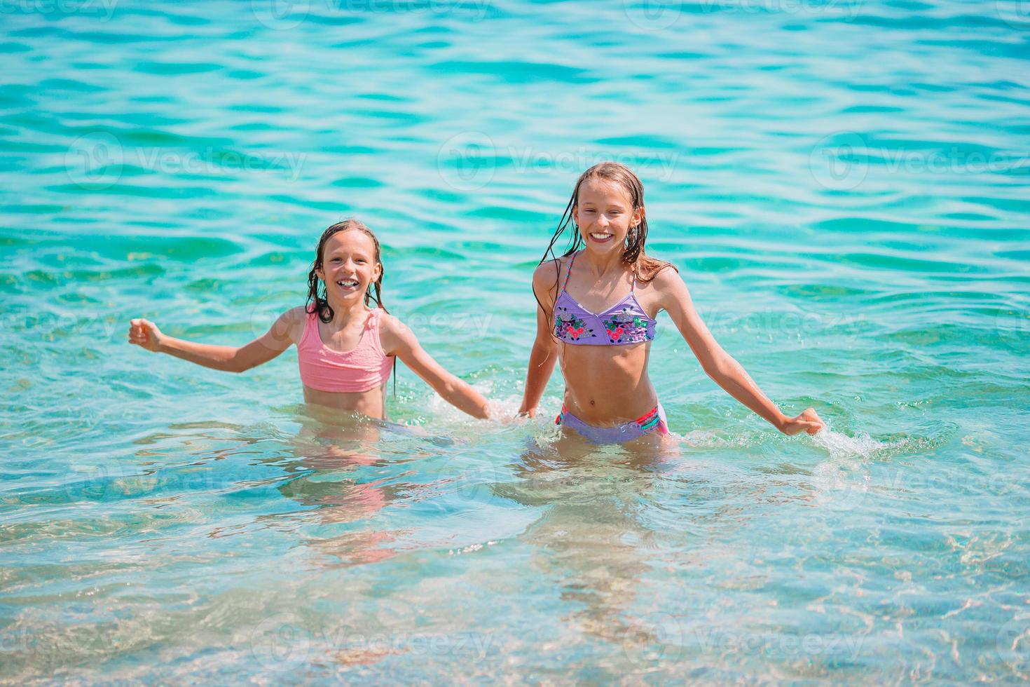 niños felices chapoteando en las olas durante las vacaciones de verano en la playa tropical. las niñas juegan en el mar. foto