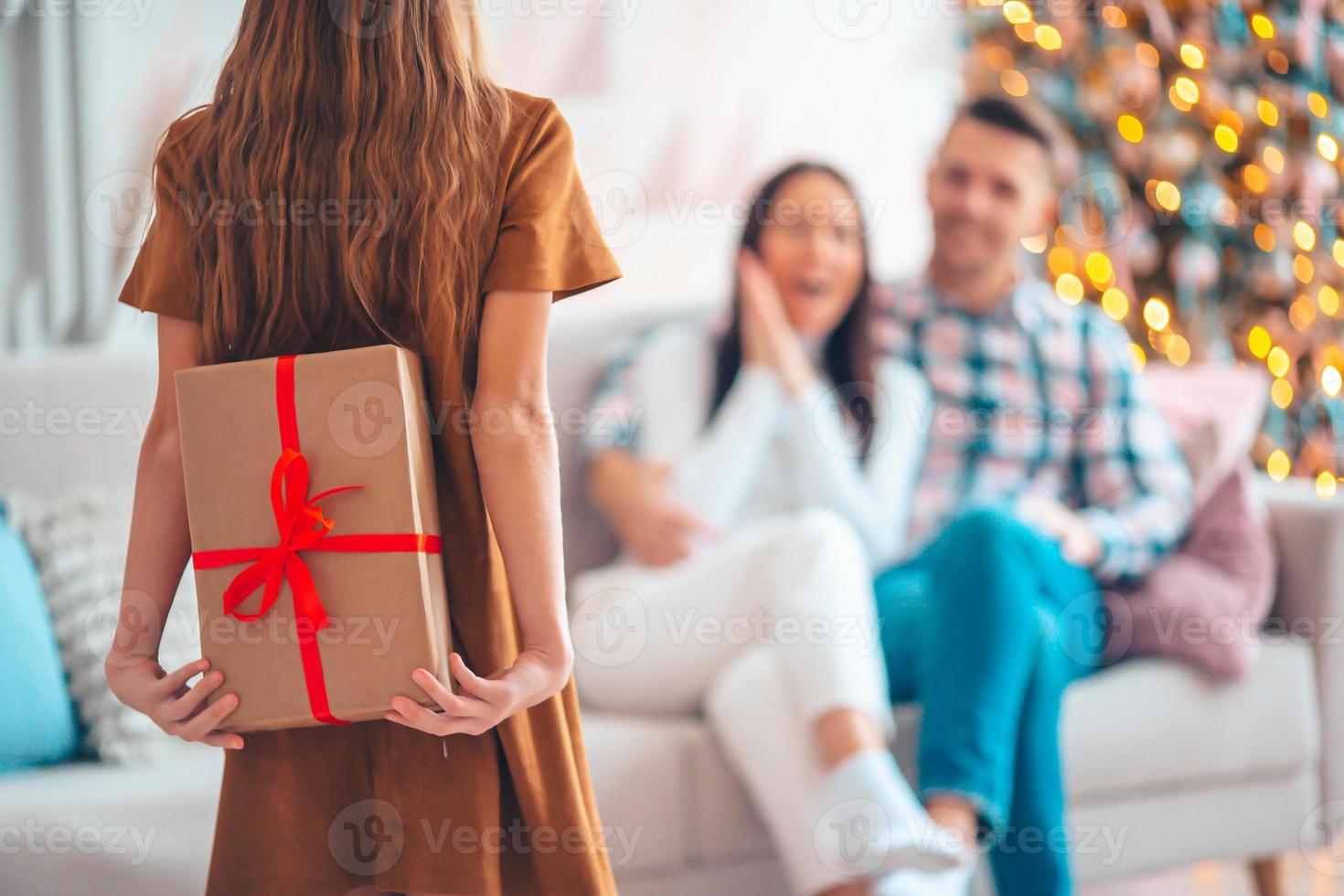Back view of kid holds a gift box near the Christmas tree indoors. photo
