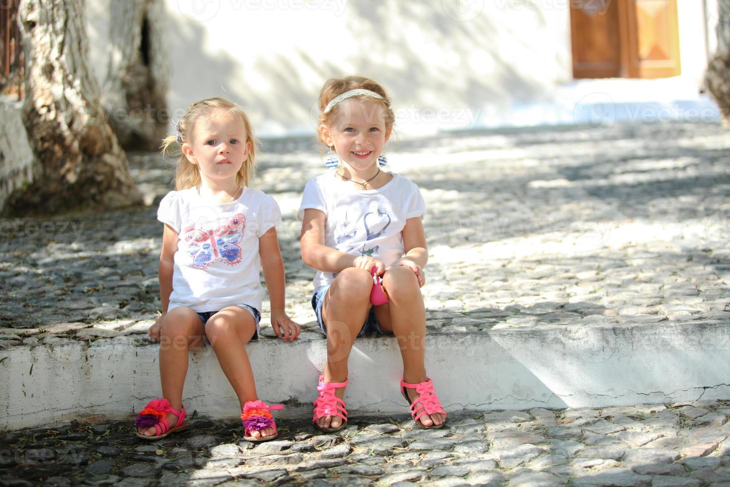 Little cute sisters sitting at street in old Greek village of Emporio, Santorini photo