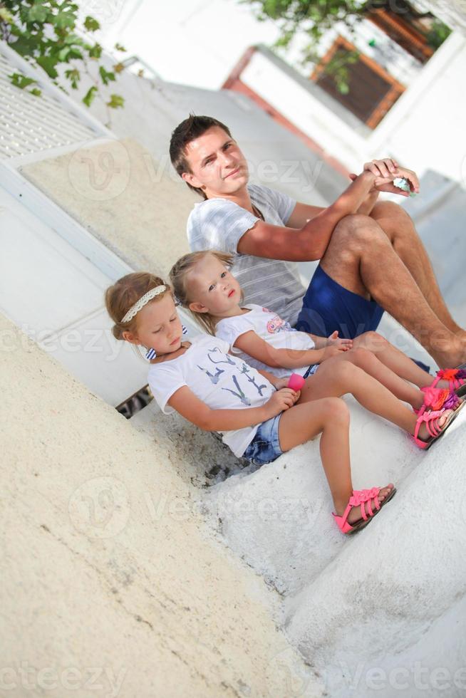 Happy father and cute daughters sitting on street in old greek town photo