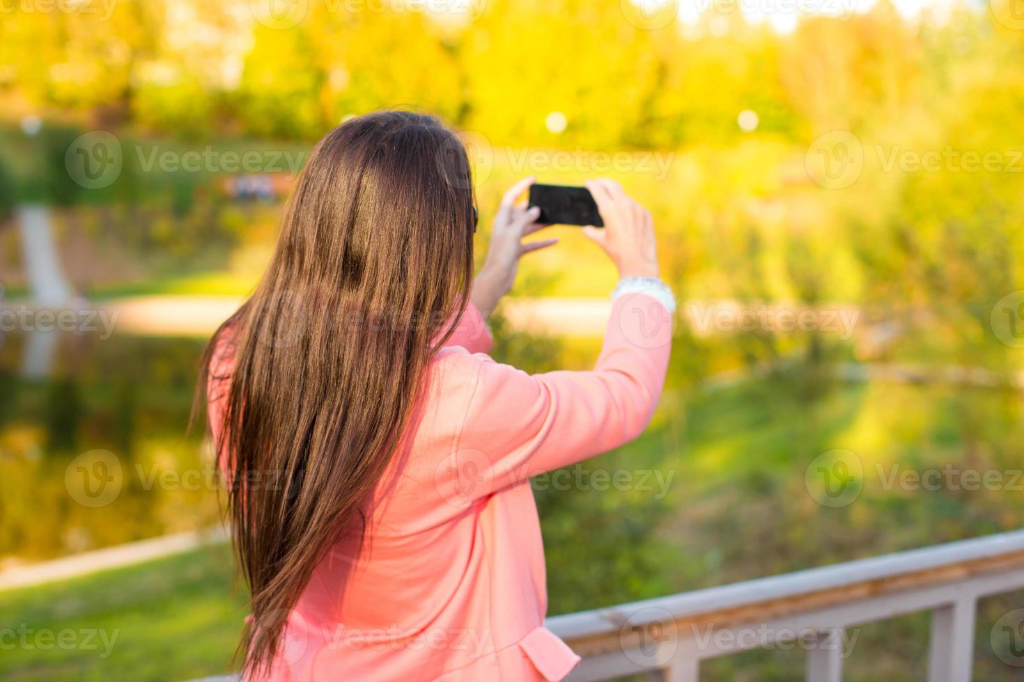 Young woman take a photo by her phone at autumn day
