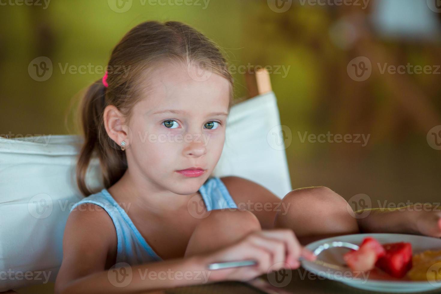 Adorable little girl having breakfast in outdoor cafe photo