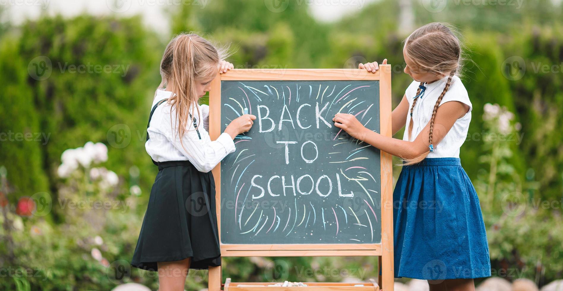 Happy little schoolgirls with a chalkboard outdoor photo