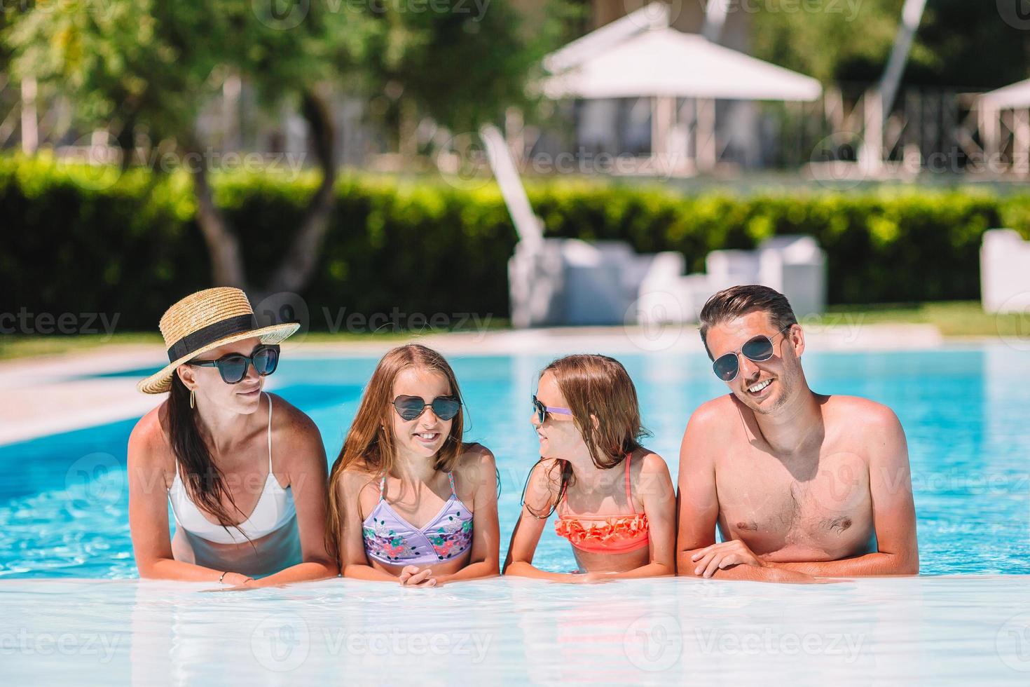 Happy family of four in outdoors swimming pool photo