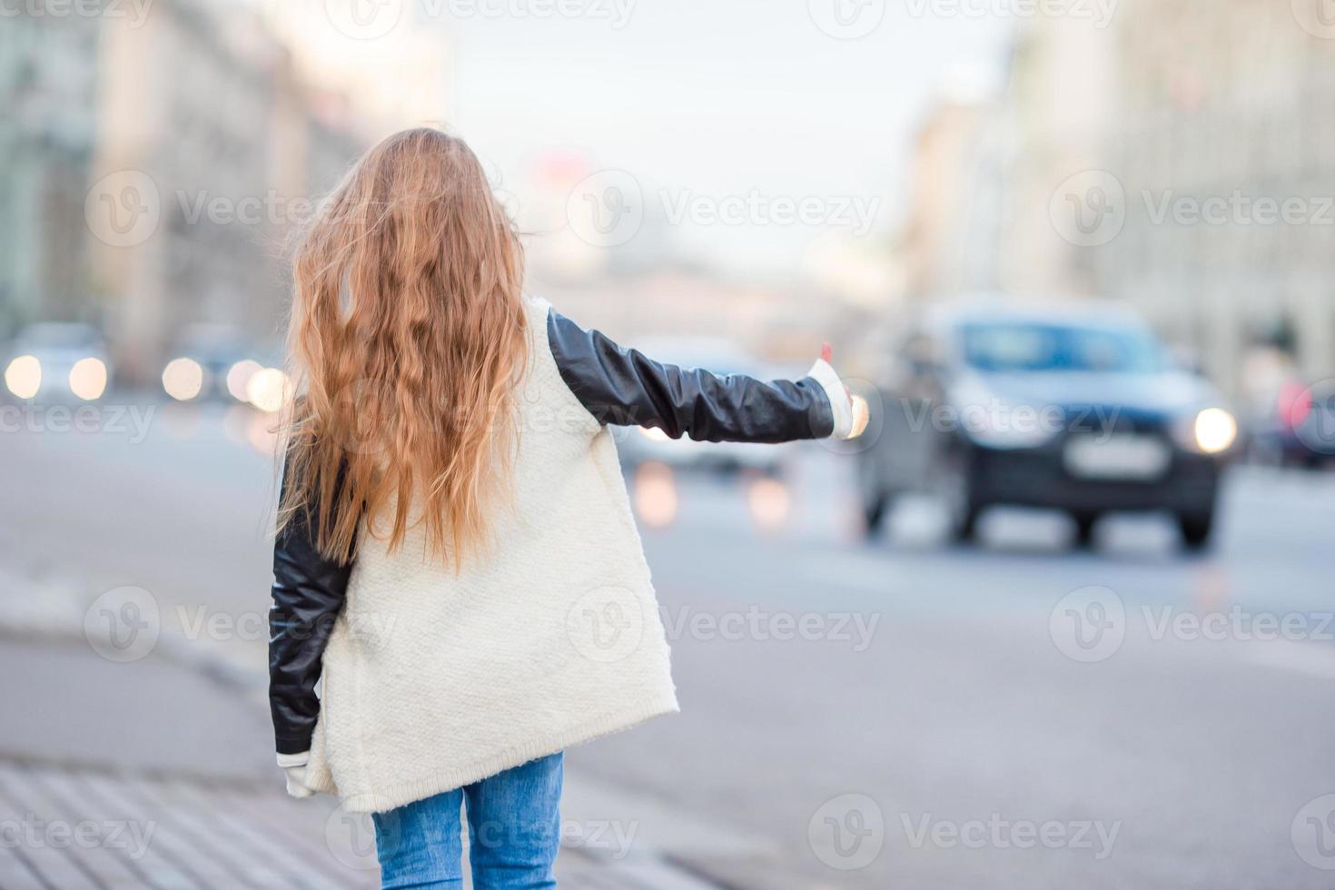 Una niña adorable toma un taxi al aire libre en una ciudad europea foto