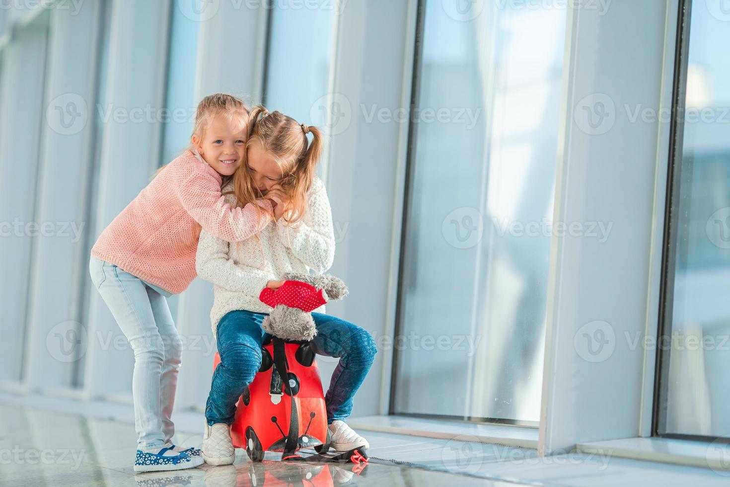 Adorable little girls having fun in airport sitting on suitcase waiting for boarding photo