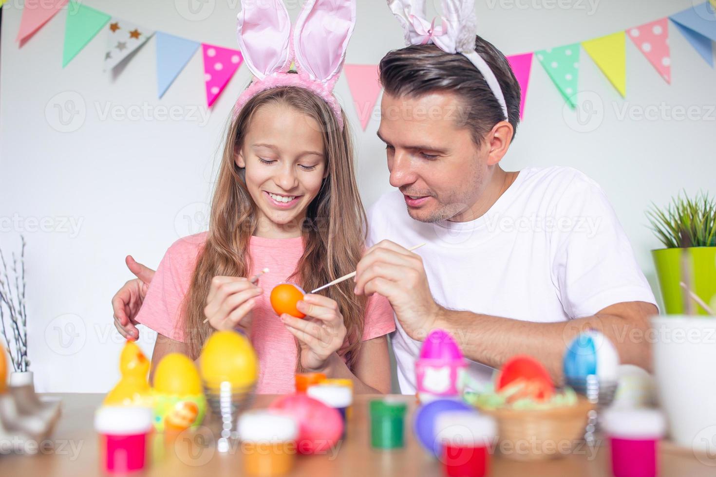Father and his little daughter painting eggs. Happy family preparing for Easter. photo