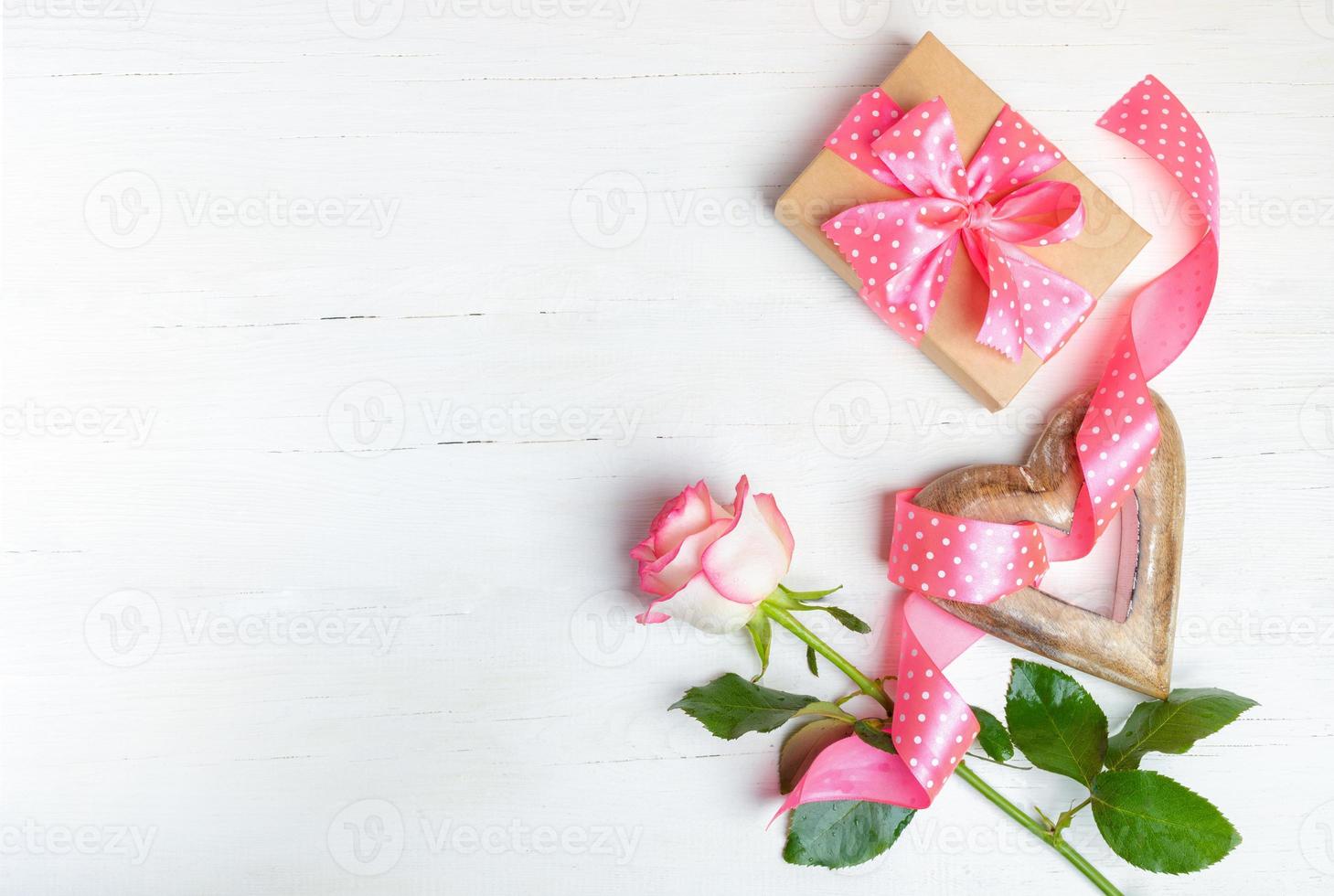 Gift, wooden heart, pink rose, polka dots ribbon on wooden white background. Top view, copy space. photo