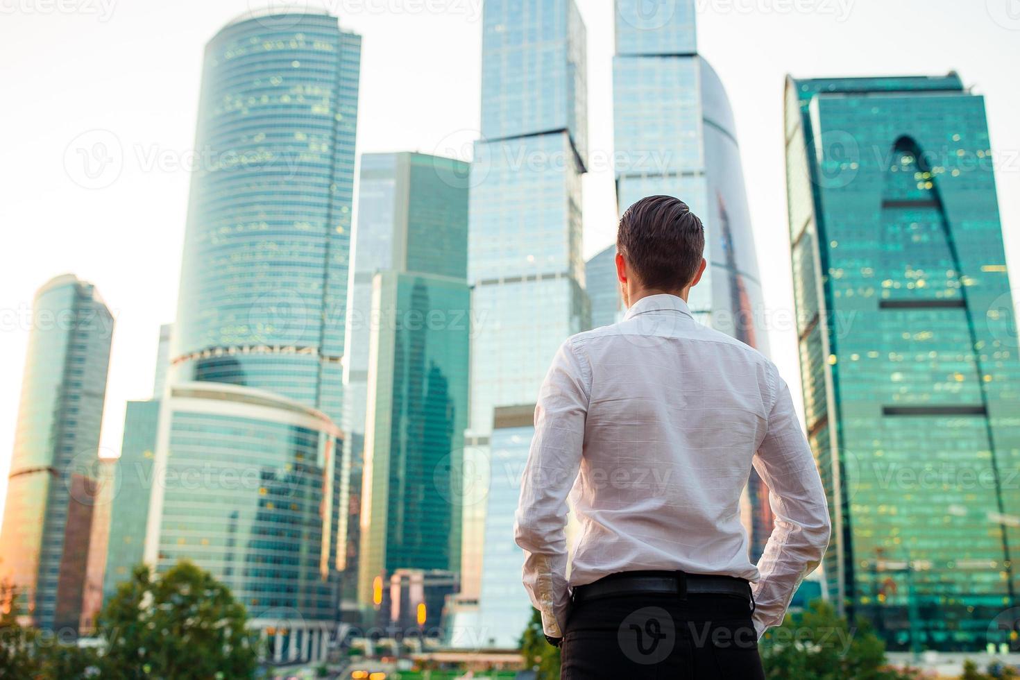 Back view of businessman looking on copy space while standing against glass skyscraper photo