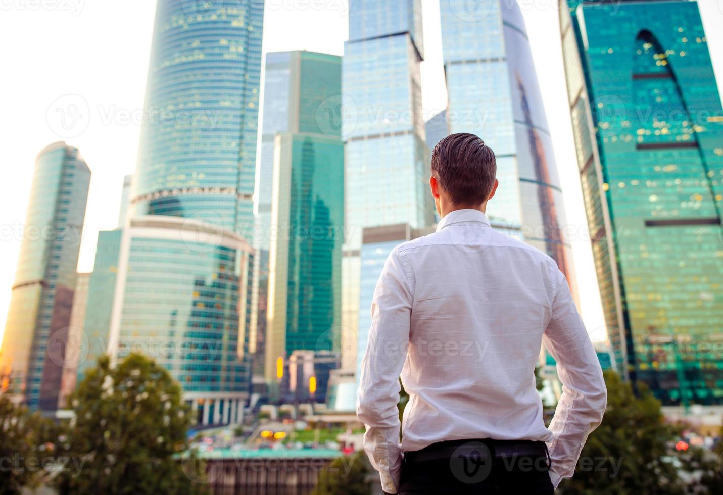 Back view of businessman looking on copy space while standing against glass skyscraper photo